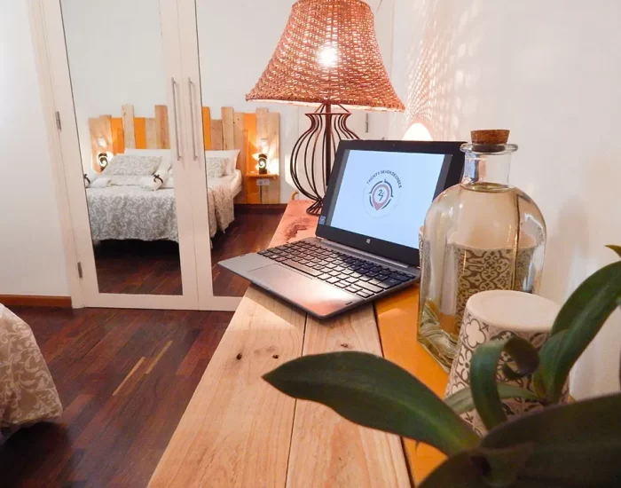 Escritorio moderno con laptop, lámpara de mimbre y decoración elegante en un dormitorio acogedor. Se refleja el ambiente cálido y funcional del espacio, ideal para trabajar o relajarse.